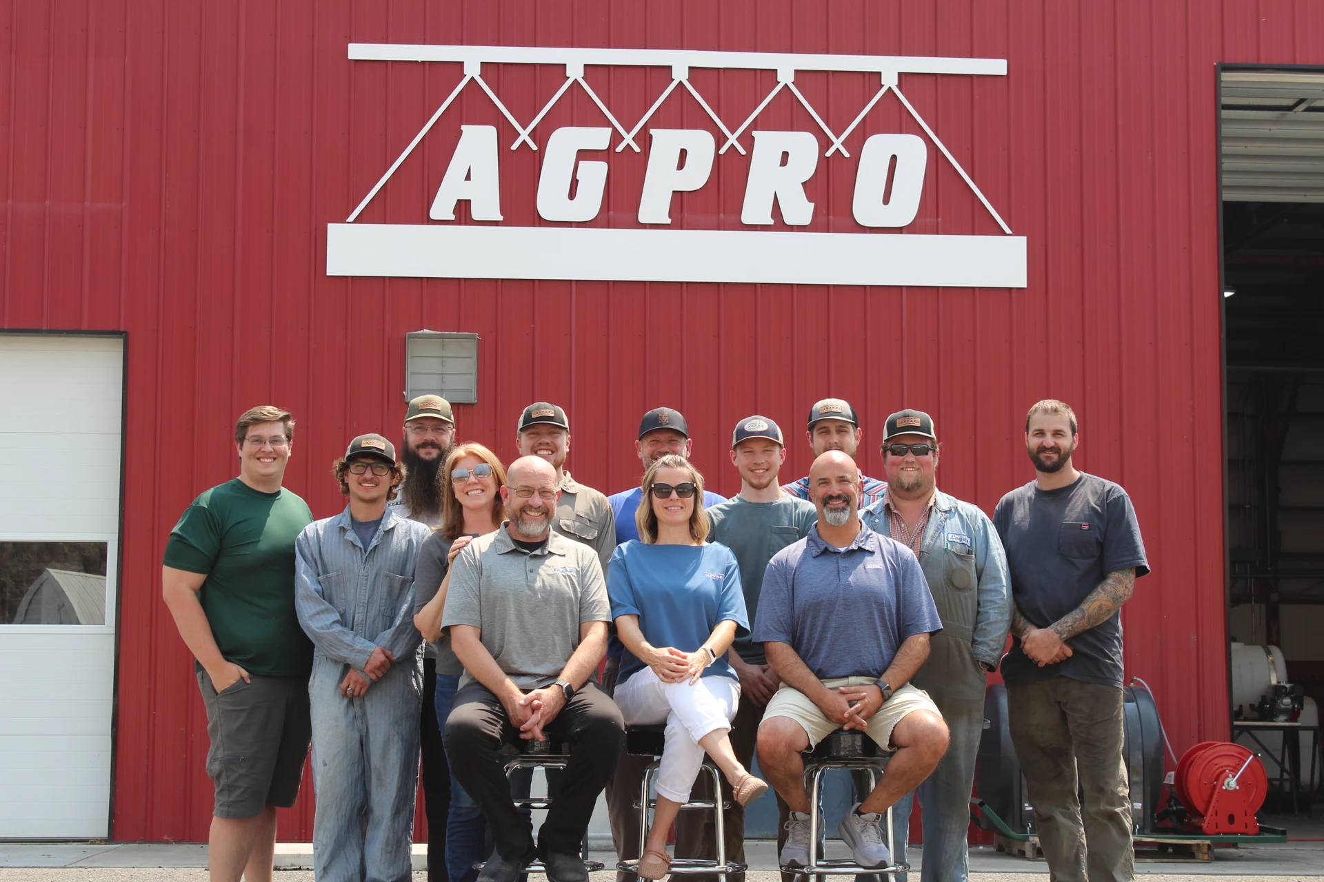 AGPRO staff gathered outside the red shop building beneath the AGPRO sign AGPRO staff gathered outside the red shop building beneath the AGPRO sign